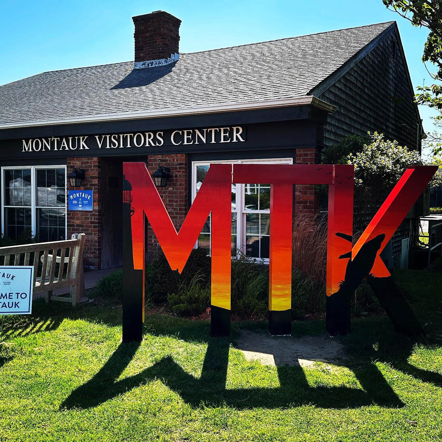Finished MTK sign by Angela Filangeri, 2023, painted red, orange, yellow sunset with black Montauk Point Lighthouse and humpback whale jumping black silhouettes