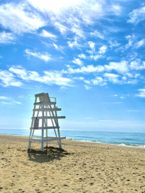 'A lifeguard chair on bright sand against a blue sky and gentle waves at South Edison Beach in Montauk