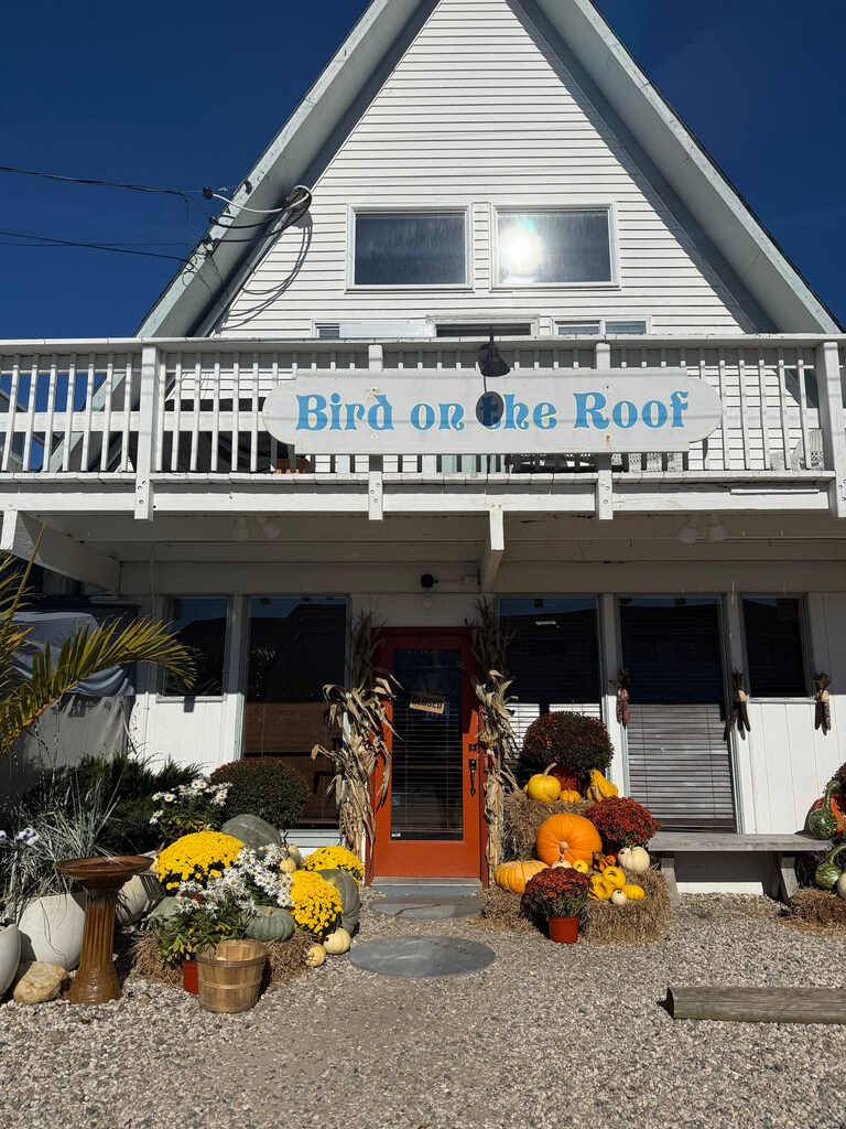 Image of the front of the Bird on the Roof Restaurant, with an orange door, and beautiful mum, pumpkin, and haybail display.